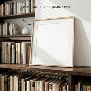 May include: A square wooden picture frame with a white mat board, featuring the text FRAME MOCKUP SQUARE PSD at the top. The frame is positioned on a dark wooden shelf, with a white wall behind it and rows of books visible on the shelves.