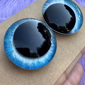 May include: Two round, glass-like eyes with a black pupil and a blue iris. The irises have a swirling pattern of light and dark blue. The eyes are set on a brown surface.