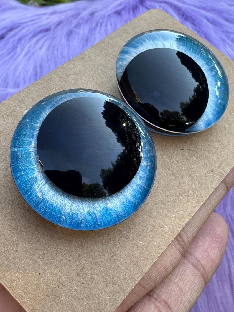 May include: Two round, glass-like eyes with a black pupil and a blue iris. The irises have a swirling pattern of light and dark blue. The eyes are set on a brown surface.