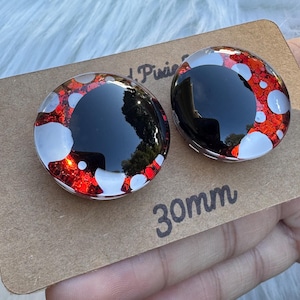 May include: Two round, glossy, black and red earrings with white accents. The earrings are 30mm in diameter (approx. 3cm). The earrings are held on a brown card.