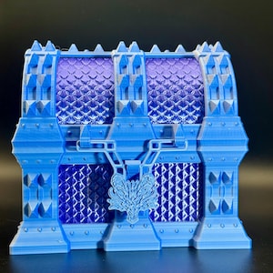 May include: A blue decorative chest with a dragon emblem on the front. The chest has a textured design and a purple interior. The chest is made of a light blue material and has a medieval theme.
