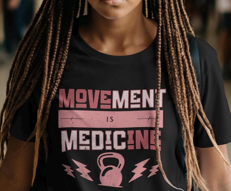 Pode incluir: Camiseta preta com o texto "MOVEMENT IS MEDICINE" em letras rosa e brancas. Um haltere rosa e um raio gr&aacute;fico est&atilde;o abaixo do texto. A camiseta tem gola redonda.