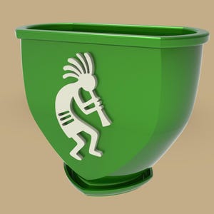 Puede incluir: Una jardinera verde con un dise&ntilde;o de Kokopelli blanco. La jardinera tiene una forma redondeada con una base plana y un borde alrededor de la parte superior. La figura de Kokopelli toca la flauta.