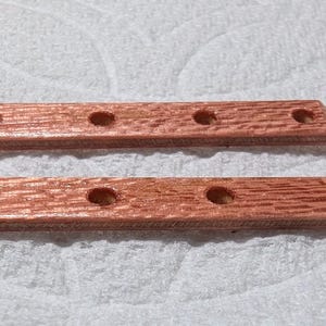May include: Two rectangular wooden pieces with a reddish-brown finish and four evenly spaced holes. The wood grain is visible, and the edges are slightly beveled. The pieces are likely components of a larger item.
