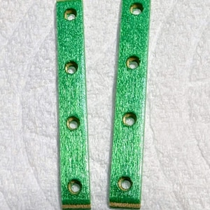May include: Two green wooden slats with four evenly spaced holes. The slats have a textured, painted finish and are rectangular in shape. The ends of the slats have a natural wood color.