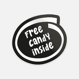 以下が含まれることがあります： 白と黒のステッカーで、白い丸みを帯びたフォントで「Free Candy Inside」というテキストが入っています。テキストは、白い境界線と白い湾曲したアクセントが付いた黒い楕円形の中にあります。