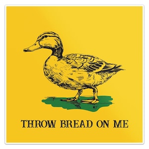 Puede incluir: Una pegatina amarilla con una ilustración en negro y amarillo de un pato. El pato está sobre una mancha verde. El texto "THROW BREAD ON ME" está impreso en negro en la parte inferior de la pegatina.