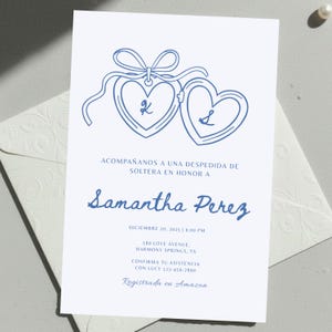 Puede incluir: Una tarjeta de invitación azul claro con un diseño de relicario en forma de corazón y las iniciales "K" y "S". La tarjeta incluye el texto "Acompáñanos a una despedida de soltera en honor a Samantha Perez" y detalles del evento.