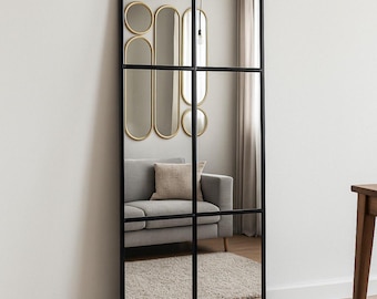 Op de afbeelding: Een grote, rechthoekige spiegel met een zwart frame en een rasterpatroon. De spiegel reflecteert een woonkamer, inclusief een grijze bank, decoratieve gouden spiegels en een beige tapijt. Een decoratief woonaccessoire.