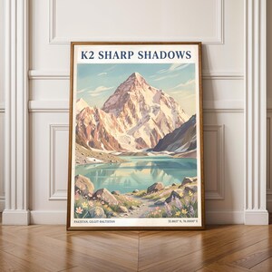 May include: A framed art print featuring a mountain landscape with a lake. The print has the text "K2 SHARP SHADOWS" at the top and the location "PAKISTAN, GILGIT-BALTISTAN" at the bottom. The artwork is in a wooden frame.