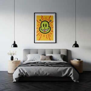 May include: A framed art print featuring a smiling green alien face with a black outline, red rays, and a yellow background. The artwork is displayed above a bed with gray bedding, two nightstands, and black pendant lights.