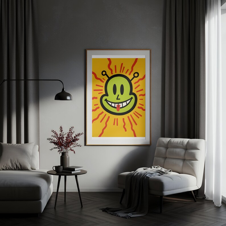 May include: A framed art print featuring a smiling green alien face with a red tongue, set against a yellow background with red sun rays. The artwork is displayed in a living room setting, adding a pop of color to the space.