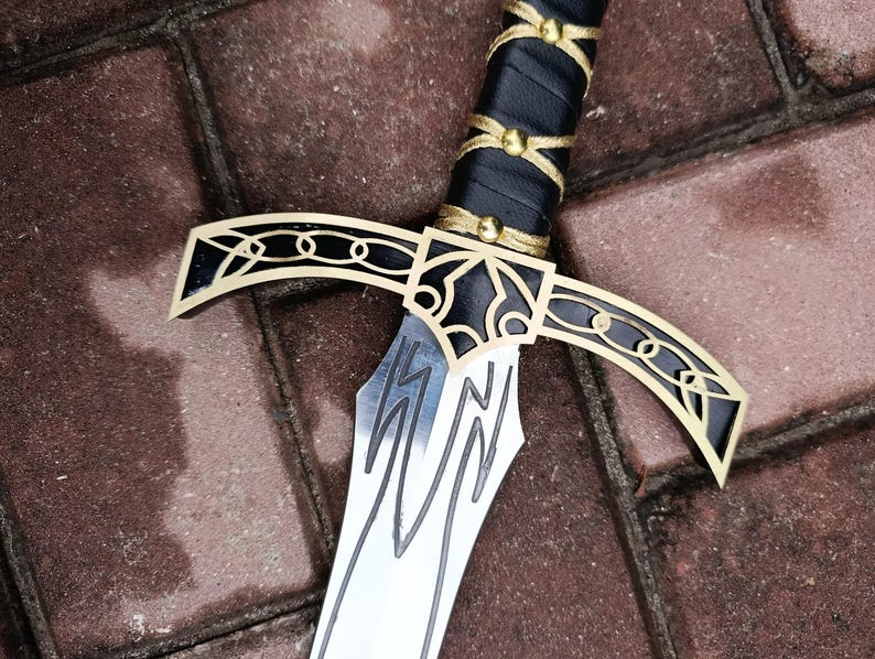May include: A close-up of a decorative sword with a silver blade and a black handle wrapped in leather. The hilt features gold accents and a stylized design. The sword is set against a brick background.