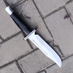 May include: A hunting knife with a polished, silver blade and a black handle. The knife has a silver bolster and a silver cap on the end of the handle. The blade is curved and has a sharp point.