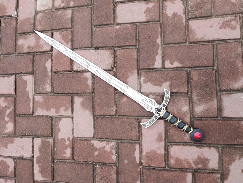 May include: A decorative sword with a silver blade and intricate designs. The hilt is black with gold accents and a red gem at the pommel. The sword is lying on a brick surface.