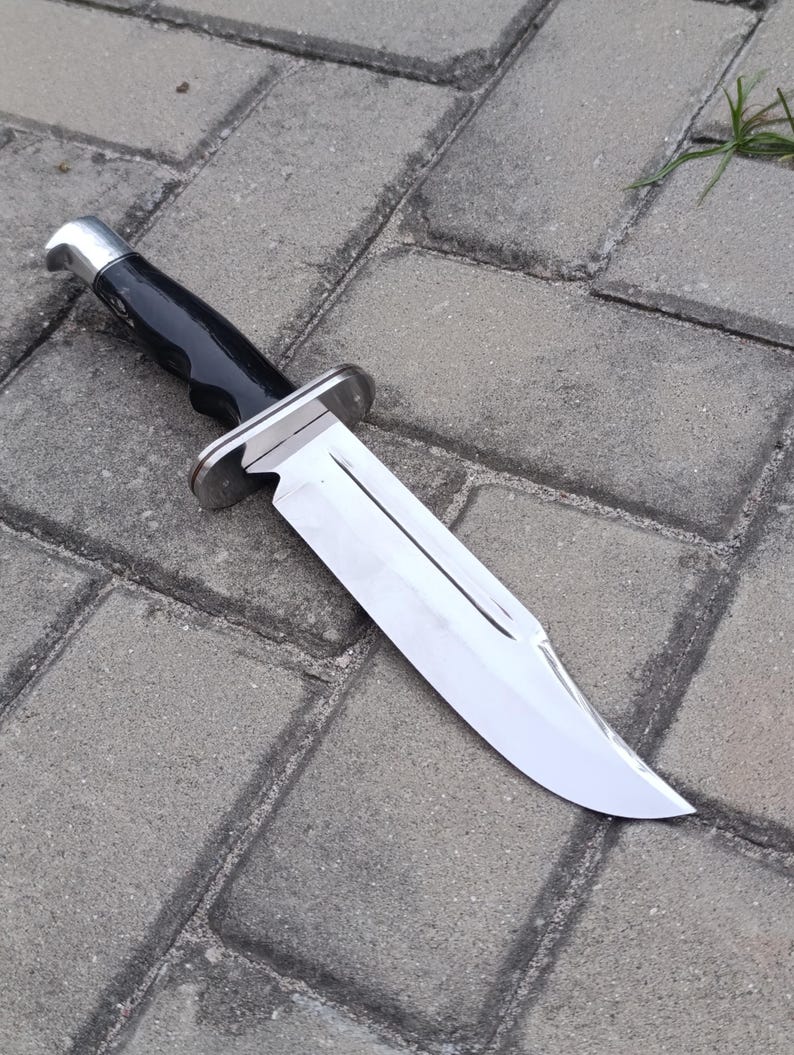 May include: A large, polished hunting knife with a shiny, silver blade and a black handle. The knife has a silver bolster and a curved blade. The handle is smooth and appears to be made of a durable material.