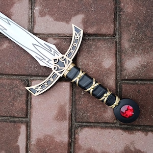 May include: A decorative sword with a silver blade and intricate gold and black detailing. The hilt is black with gold accents and a red gem at the pommel. The sword is lying on a brick surface.