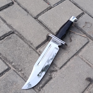 May include: A large, shiny hunting knife with a polished steel blade and a black handle. The knife features a silver bolster and a full tang construction. The blade is approximately 8 inches long.