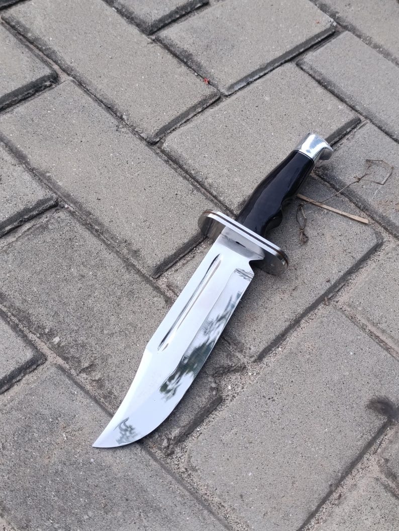 May include: A large, shiny hunting knife with a polished steel blade and a black handle. The knife features a silver bolster and a full tang construction. The blade is approximately 8 inches long.