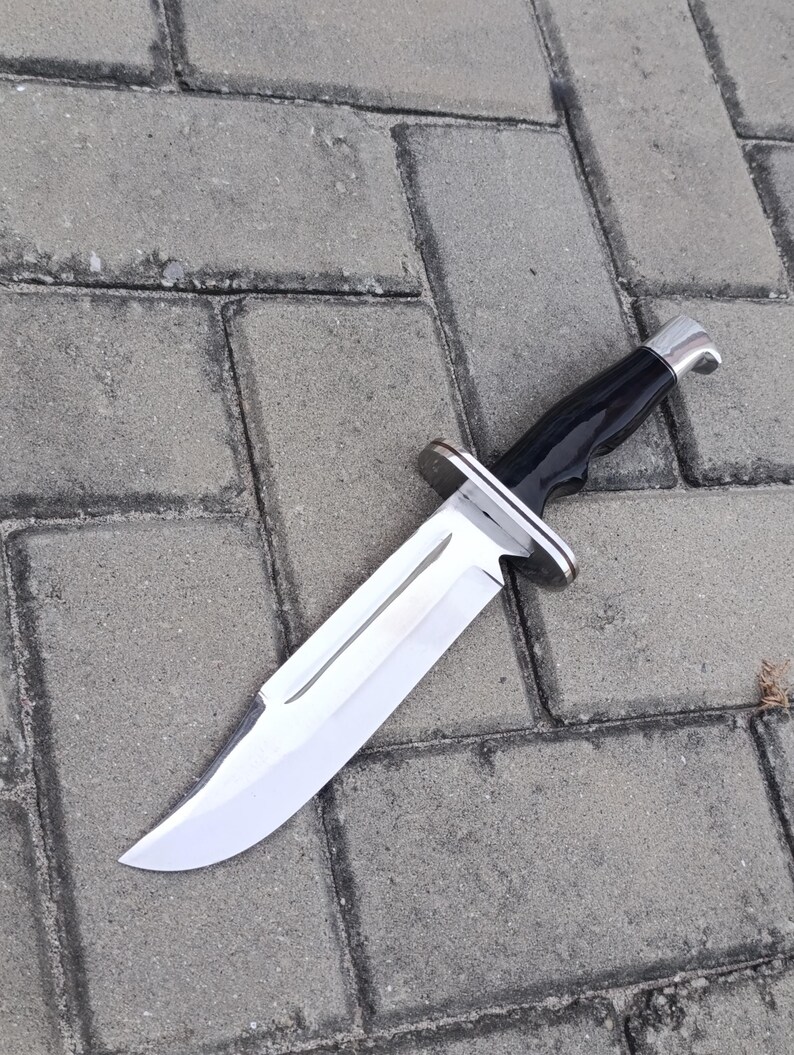 May include: A large hunting knife with a polished, silver blade and a black handle. The knife features a silver bolster and a curved blade, designed for outdoor use and survival.