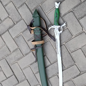 Puede incluir: Una espada de fantas&iacute;a verde y plateada con una hoja curva, junto a una vaina verde a juego. La espada tiene una empu&ntilde;adura verde decorativa y una guarda plateada. La vaina est&aacute; asegurada con correas de cuero marr&oacute;n.