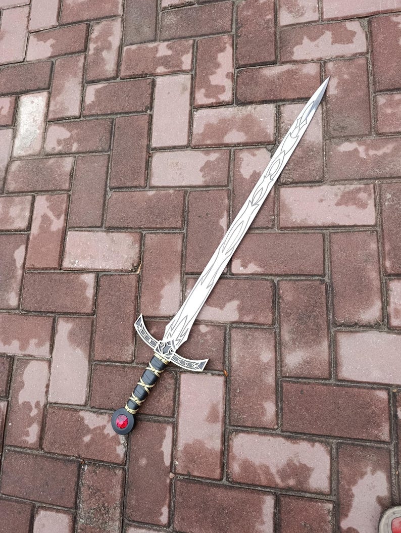 May include: A silver sword with a decorative hilt and a red gem at the base of the handle. The blade has etched designs. The handle is black and gold. The sword is lying on a brick surface.