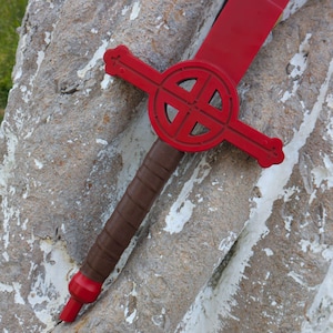 May include: A toy sword featuring a bright red blade and a matching red crossguard with a circular cutout design. The handle is brown with a textured, wrapped appearance, ending in a red pommel. The sword is constructed from smooth plastic.