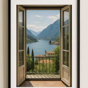 May include: Framed print of a scenic view through an open window. The image captures a serene lake surrounded by mountains, with a balcony and buildings in the foreground. The window frame is light brown, and the print is in a black frame.
