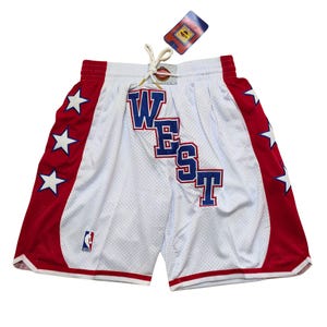 May include: White mesh basketball shorts with red and blue detailing. The shorts display the word "WEST" in blue block letters, red side panels with white stars, and an NBA logo.