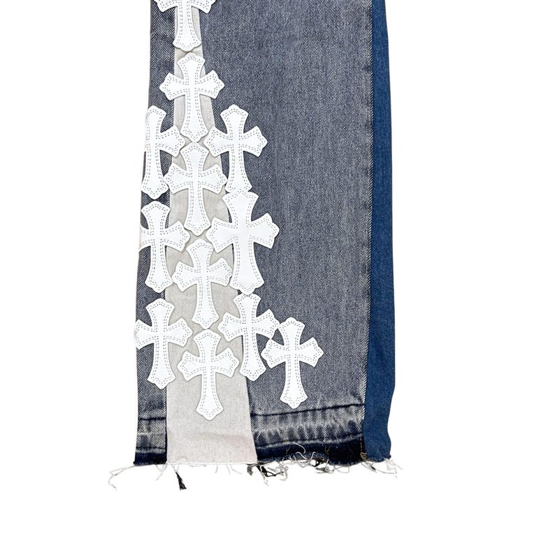 May include: Close-up of denim jeans with white cross appliques. The jeans have a distressed look with frayed edges and a mix of light and dark blue denim. The crosses are evenly spaced along the side.