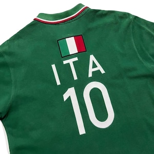 Pu&ograve; includere: Polo verde con la toppa della bandiera italiana, le lettere "ITA" e il numero "10" in bianco. Il colletto ha strisce rosse e bianche. La maglia &egrave; realizzata in materiale morbido.