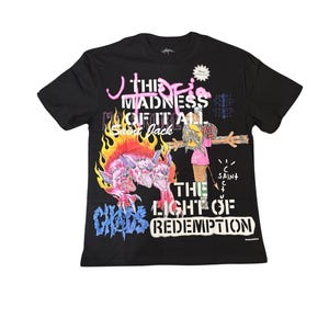 May include: Black t-shirt with a colorful graphic design. The design includes text that reads "THE MADNESS OF IT ALL" and "THE LIGHT OF REDEMPTION". A cartoon-like figure is depicted with flames and other illustrations.