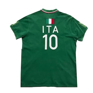Pu&ograve; includere: Polo verde a maniche corte con la bandiera italiana e la scritta "ITA" sopra il numero "10" in bianco. Il colletto ha una striscia verde, bianca e rossa. La maglia ha una piccola toppa su ogni manica.