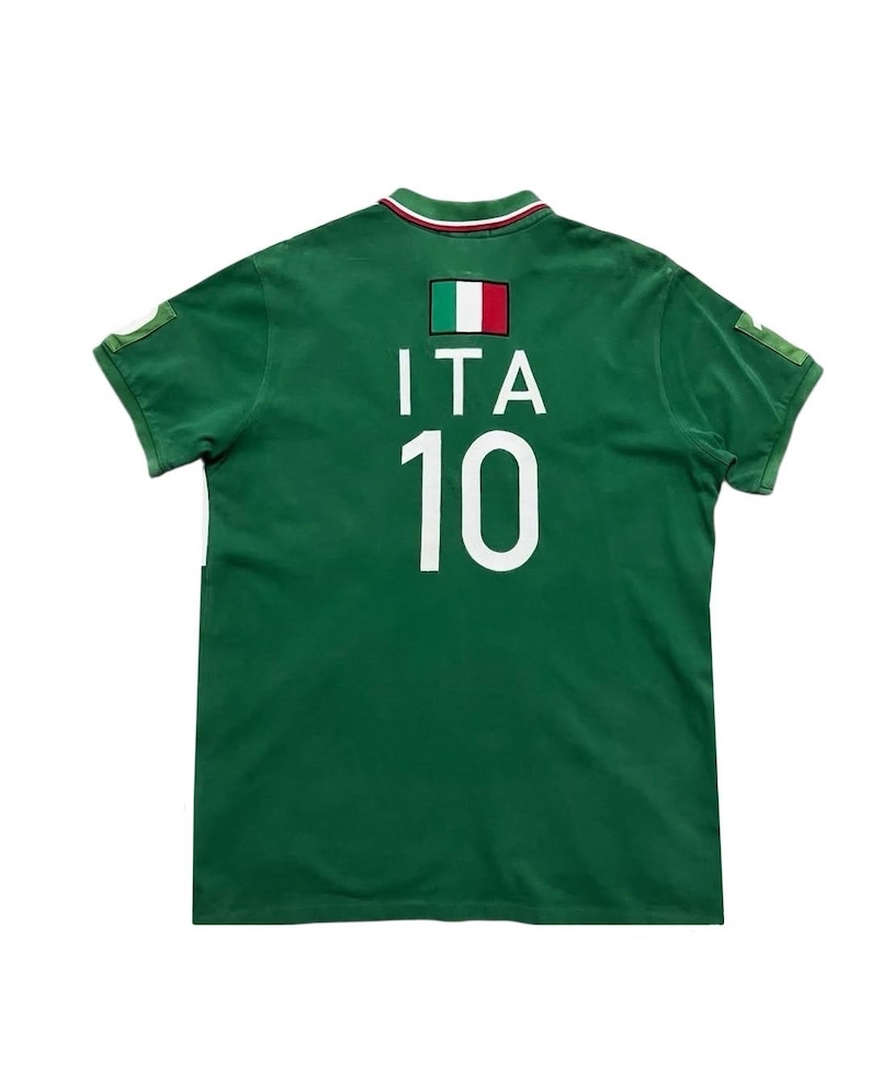 Pu&ograve; includere: Polo verde a maniche corte con la bandiera italiana e la scritta "ITA" sopra il numero "10" in bianco. Il colletto ha una striscia verde, bianca e rossa. La maglia ha una piccola toppa su ogni manica.