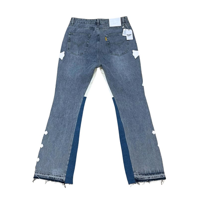 May include: Faded blue denim jeans with white and dark blue accents. The jeans have a classic five-pocket design, a frayed hem, and white patches. A tag is attached to the back pocket.