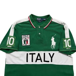 Pu&ograve; includere: Polo verde con dettagli bianchi e la scritta "ITALY" sul petto. Presenta il numero "10" sulle maniche e un logo bianco ricamato di un giocatore di polo. Include una piccola toppa con testo.