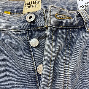 May include: Close-up of blue denim jeans with visible stitching and silver button closures. The jeans feature the "GALLERY DEPT." label. The denim has a faded, worn appearance.