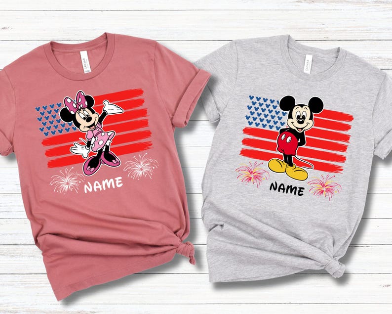 May include: Two short-sleeved t-shirts, one dusty rose and one heather gray. Each shirt features a cartoon character design with an American flag motif, fireworks, and the word "NAME" printed below the design.