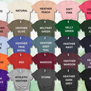 May include: A collection of t-shirts in various colors, each labeled with its color name in white text. Colors include white, natural, peach, pink, and raspberry, among others. The shirts are arranged in rows, showcasing a wide range of options.