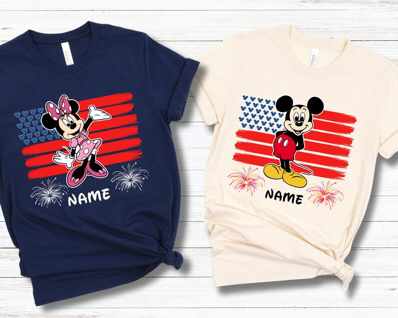 May include: Two t-shirts featuring cartoon characters in front of an American flag design. One shirt is navy blue with Minnie Mouse, the other is cream-colored with Mickey Mouse. Both shirts have the word "NAME" printed below the characters.