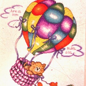 May include: A colorful hot air balloon with a basket holding a kitten, embroidered on fabric. The balloon is in shades of yellow, red, blue, and purple. The text "June 15, 2014" and "3 lbs. 2 oz." are included. The name "Cameron Jordyn" is at the bottom.