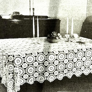 May include: A white, crocheted tablecloth with a floral pattern covers a table. The table is set with candles and a small bowl of flowers. The tablecloth has a scalloped edge and a detailed, openwork design.