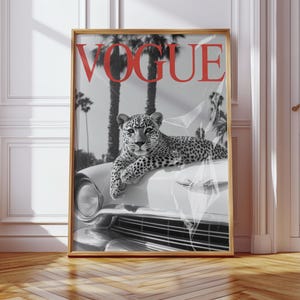 May include: Framed print featuring a black and white image of a leopard resting on a classic car. The word "VOGUE" is displayed in red at the top. Palm trees are visible in the background, creating a vintage, stylish aesthetic.