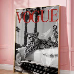 May include: A framed print featuring a black and white image of a leopard resting on a white car. The word "VOGUE" is in red at the top. Palm trees are in the background. The frame is gold.