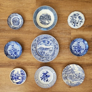 May include: A collection of eight ceramic plates and bowls featuring blue and white transferware patterns. The designs include various landscape scenes, floral motifs, and intricate border details arranged in a grid on a flat surface.