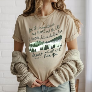 May include: Beige t-shirt with a green and white mountain graphic and the text "for the mountains may depart and the hills be removed, but my steadfast love shall not depart from you." A casual, everyday tee.