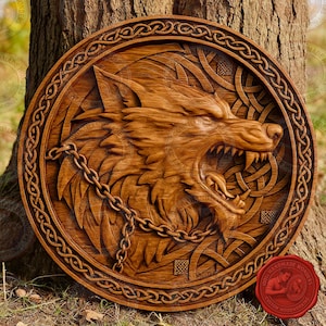 Op de afbeelding: Ronde houten sculptuur van een brullende wolfskop met ketting, omringd door Keltische knoopwerk en een decoratieve rand. Het hout heeft een warme, bruine tint.