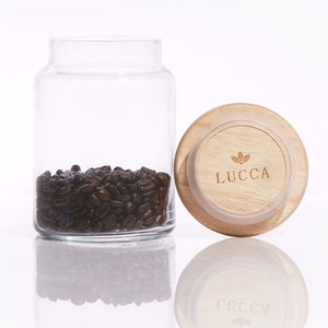 May include: A glass jar with a wooden lid filled with coffee beans. The lid has the word "LUCCA" printed on it.