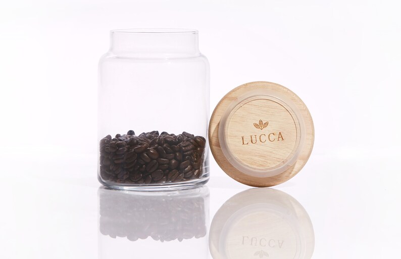 May include: A glass jar with a wooden lid filled with coffee beans. The lid has the word "LUCCA" printed on it.