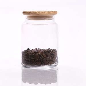 May include: A clear glass jar with a wooden lid filled with dark brown coffee beans.